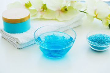 Obraz na płótnie Canvas Blue Bath Salt, Body Cream and Shells For Spa on White Table Background