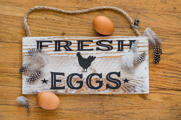 Wooden sign that says fresh eggs with feathers and brown eggs
