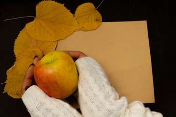 Woman's hand in a sweater holds a cup of apple on the background of an envelope with jagged leaves, an autumnal mood, an empty space for the text.