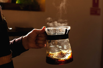 barista holds a drink in hand with a steam making alternative way of brewing coffee in the coffee shop hario v60 soft light background