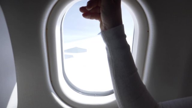 POV, CLOSE UP: Unrecognizable woman opens the airplane window and lets blinding light into cabin, revealing a stunning view of the bright blue sky. Awesome shot of modern aircraft wing and cloudy sky.