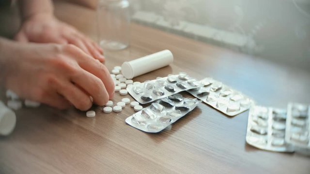 Closeup man's hands takes tablets and pills from the table.