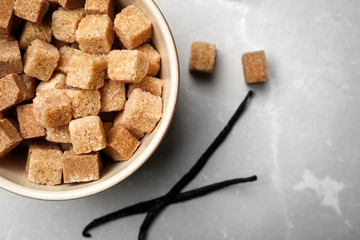 Bowl of aromatic vanilla lump sugar and sticks on grey background