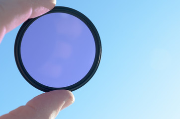 Fingers hold the photo filter against the blue sky.