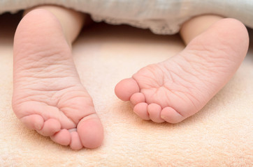 Baby feet from under the blanket on the bed.