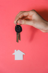 Human Hand Holding Key to Dream Started House against Pink Background.