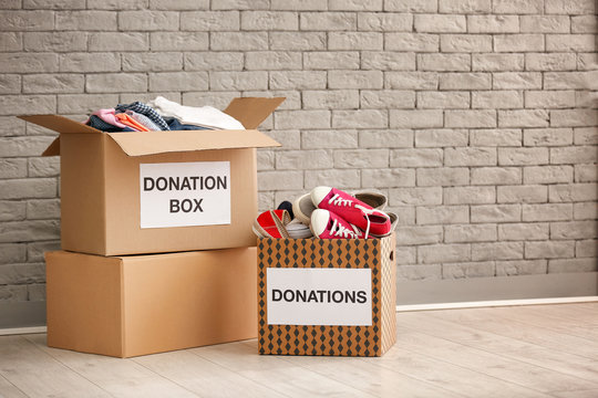 Donation boxes with clothes and shoes on floor against brick wall