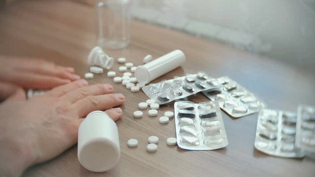 Men's hands slip off the table with white pills, blisters and tablets.