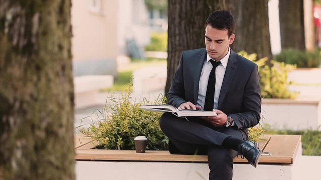 Young Business Man Reading Book While Drinks Coffee Outdoor