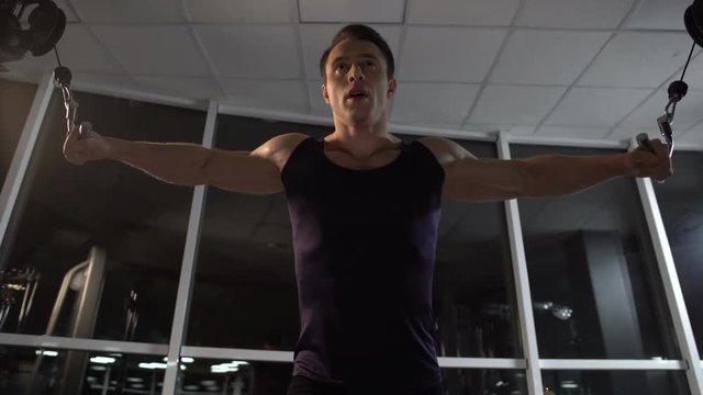 Bodybuilder training chest muscles, doing cable fly exercise, achieving goal