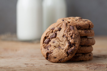 A stack of cookies with milk chocolate and two bottles of milk on a wooden table