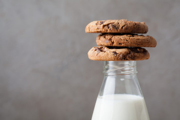 Bottle with milk and chocolate chip cookies on dark background with copy space