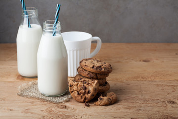 Two bottles of milk and chocolate chip cookies on dark background with copy space