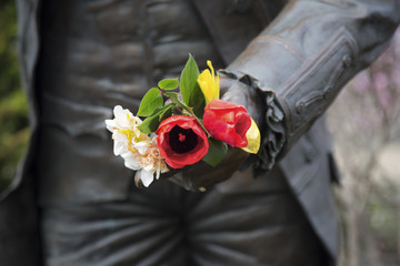 Partial view of a bronze 18th century statue of a man, in his hand a small real fresh flower bouquet - off center frame