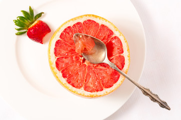 Overhead view of ruby red grapefruit with spoon in a white plate