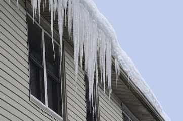 Close up of a house with snow covered roof and long icicles hanging from the eaves-through and gutter