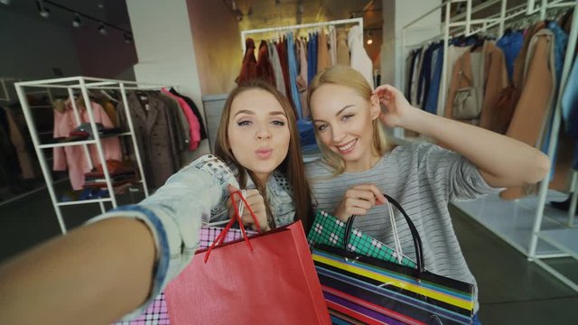 Point of view shot of two beautiful young women making selfie with paper bags in women's clothing department. Girls are posing, laughing and chatting happily