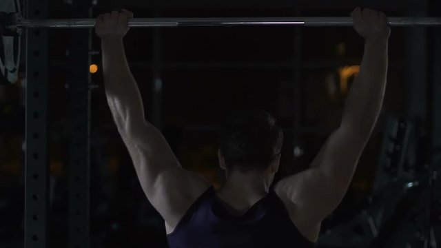 Muscular man lifting barbell in gym slow-mo, evening workout, sport motivation