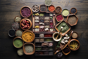 Variety of colorful dry spices  and herbs in teakwood bowls. Rustic wooden kitchen table. Indian...