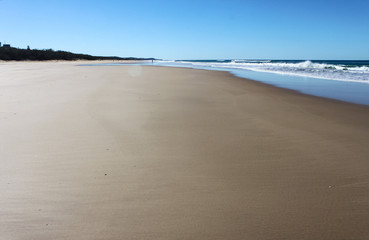 Wide beautiful expanse of beach in foreground with waves coming in and people tiny in and near the water in the background