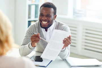 Smiling African American entrepreneur sitting at office desk and discussing details of mutually...