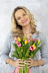 Young pretty woman with a bouquet of flowers stands in front of concrete wall and is happy about mother's day, birthday, wedding day