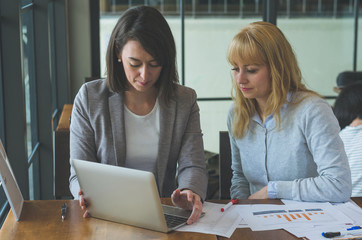 two attractive young woman working together reading and annalyst on paperwork and using laptop to mentoring about some business planning at coffee shop.