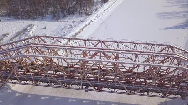 Top view suspension railway bridge for train movement over frozen river on winter landscape. Aerial view train bridge through winter river.