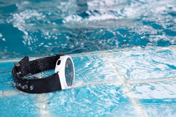 Waterproof digital wristwatch placed on the edge of the swimming pool.