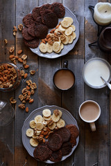 Top view of a wooden table on which are plates of biscuits, mugs of cocoa and nuts