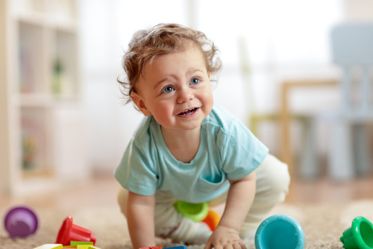 cute infant baby boy crawling on the floor at home, playing with colorful toys