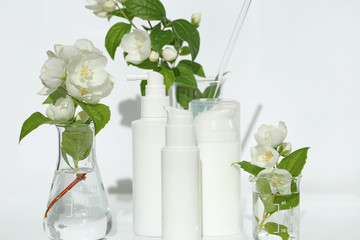 jasmine extract. cosmetics with jasmine extract in white bottles and jasmine flowers in laboratory flasks on a white background.cosmetic mockup white bottles with copy space
