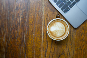 Top view of wooden desk with laptop and a coffee latte art with copy space.