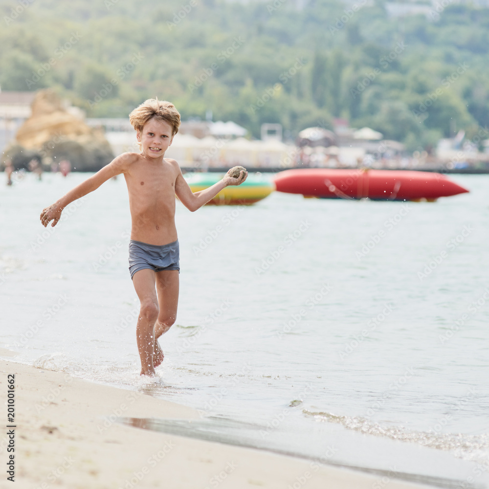 Wall mural Smiling boy enjoying summer vacation and playing on the beach, image with square aspect ratio