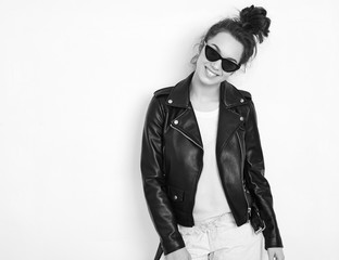 Portrait of young beautiful brunette woman girl model with nude makeup wearing summer hipster biker leather jacket clothes in sunglasses posing near wall. Going crazy