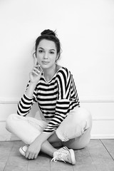 Obraz premium Portrait of young beautiful brunette woman girl model with nude makeup in summer hipster clothes posing near wall. Sitting on the floor