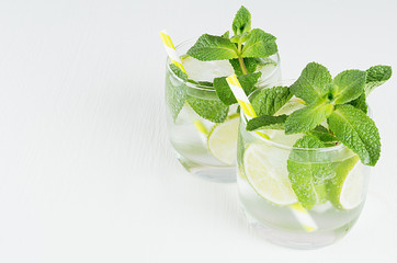 Fresh cold summer beverage mojito with lime, leaf mint, straw, ice cubes, soda on white wood...