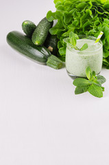 Healthy green spinach smoothies with leaf mint, greens, straw, green vegetables on white soft wood board, copy space, vertical.