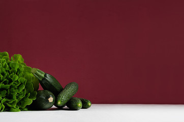 Green vegetables - salad spinach, cucumbers, zucchini on modern colorful bordo and white kitchen interior. Healthy vegeterian raw summer food ingredients.
