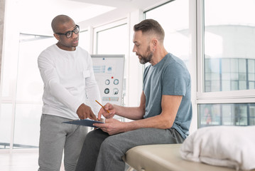 Obraz premium My diagnosis. Smart nice man pointing at the notes while showing his diagnosis to the patient