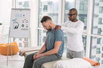 Obraz premium Muscle relaxation. Smart nice man standing behind his patient while doing a shoulder massage