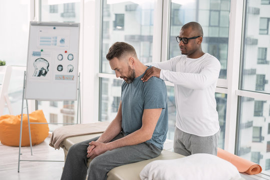 Muscle relaxation. Smart nice man standing behind his patient while doing a shoulder massage