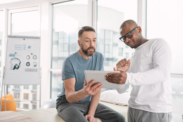 Video lesson. Joyful nice doctor standing near his patient and showing his the video on the tablet