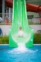 Green water slide and girl in water splashes. water attraction. Girl down the slides with a spray....