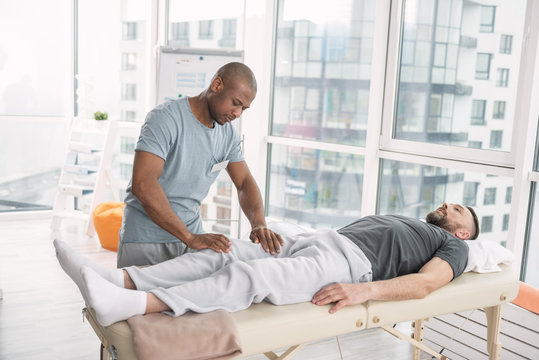 Medical massage. Smart nice man standing near his patient while doing a massage for him