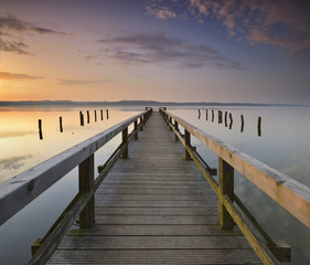 Naklejka premium Calm Lake at Sunrise, Long Wooden Pier 