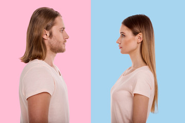 Staring competition. Charming young woman in a beige t-shirt facing her boyfriend while she standing against a blue background and the man posing against a pink background