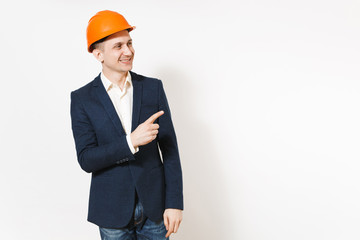 Young handsome smiling businessman in dark suit, protective hardhat pointing index finger aside on copy space isolated on white background. Male worker for advertisement. Business, working concept.