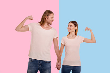More powerful together. Upbeat young woman and her boyfriend intertwining fingers and raising their arms, showing biceps, while looking at each other fondly