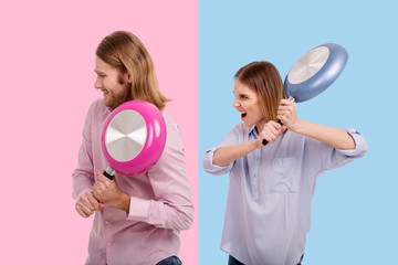 Under attack. Aggressive young woman attacking her boyfriend with a frying pan while he cowering...